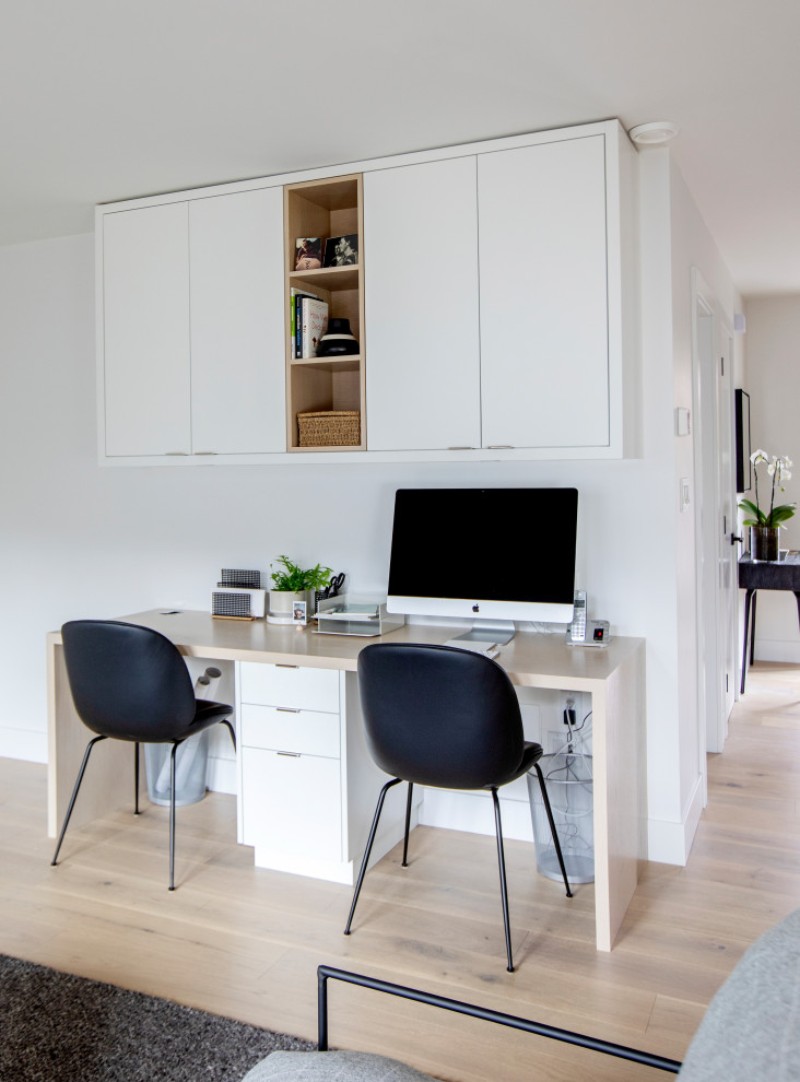Imagen de despacho moderno con paredes blancas, suelo de madera clara, escritorio empotrado y suelo beige