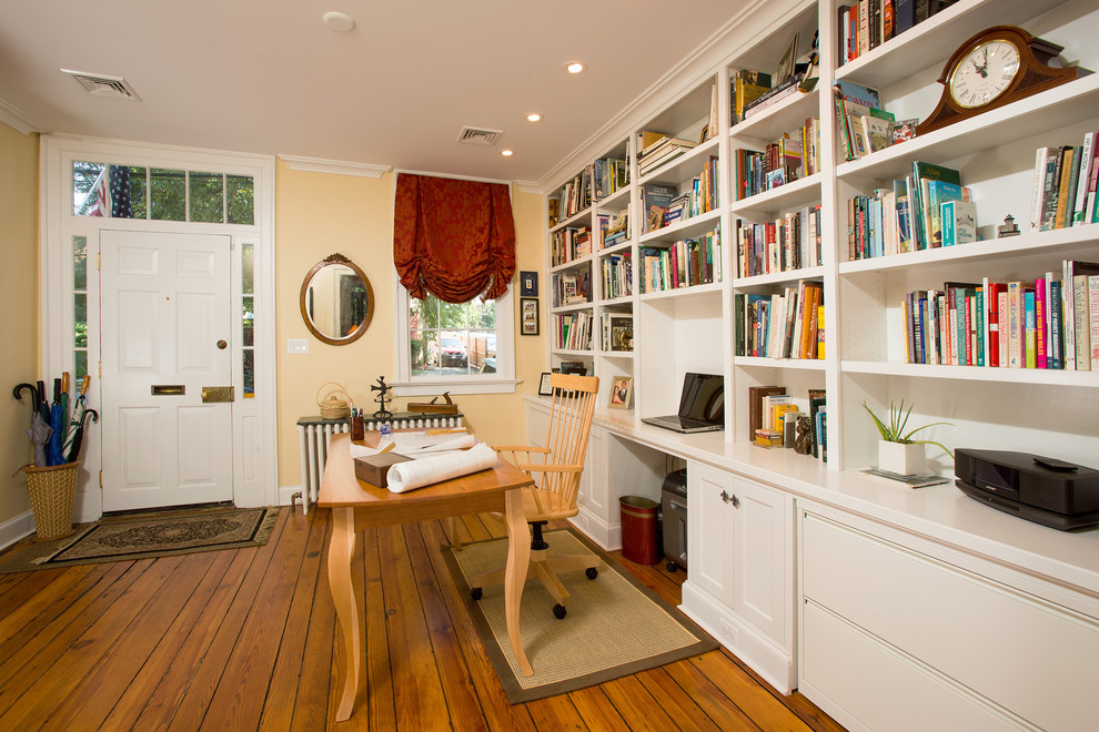 Ejemplo de despacho clásico de tamaño medio sin chimenea con paredes amarillas, suelo de madera en tonos medios, escritorio independiente y suelo marrón