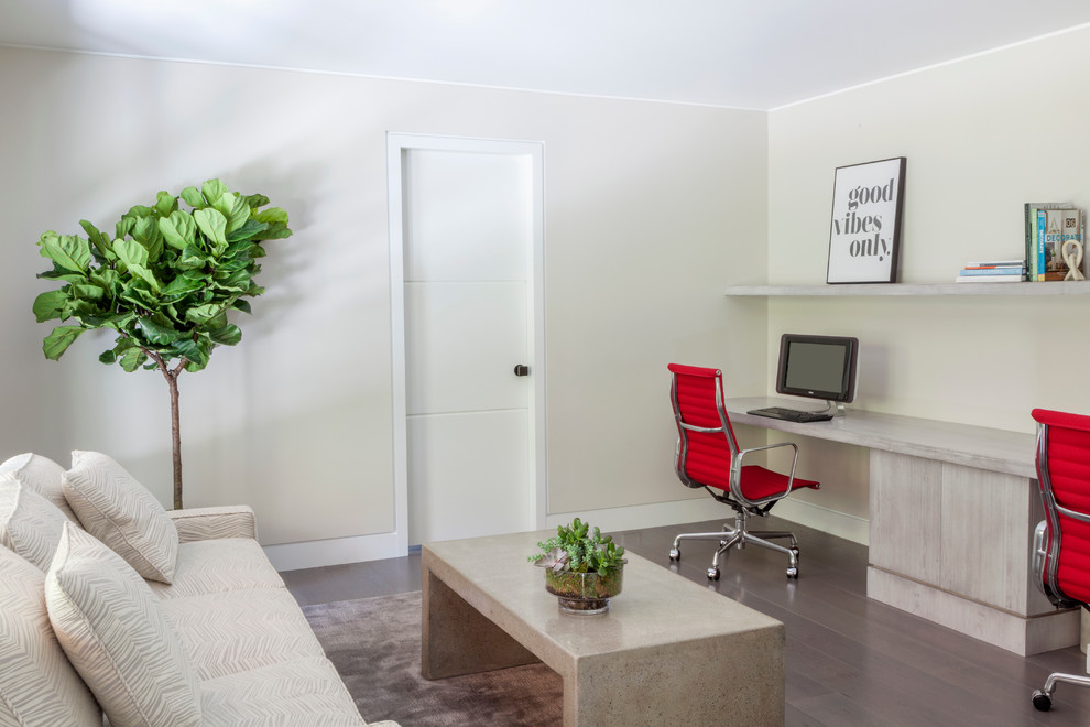 Modelo de despacho actual de tamaño medio con paredes beige, escritorio empotrado y suelo de madera oscura
