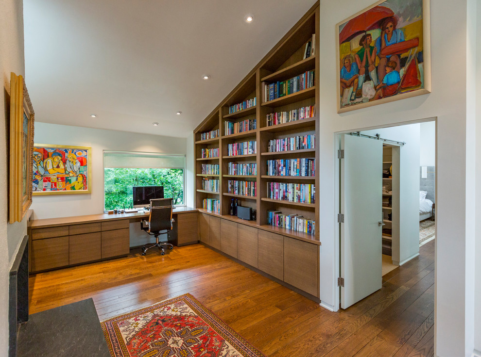 Cette photo montre un bureau moderne de taille moyenne avec une bibliothèque ou un coin lecture, un mur blanc, un sol en bois brun, une cheminée standard, un manteau de cheminée en pierre, un bureau intégré et un sol marron.