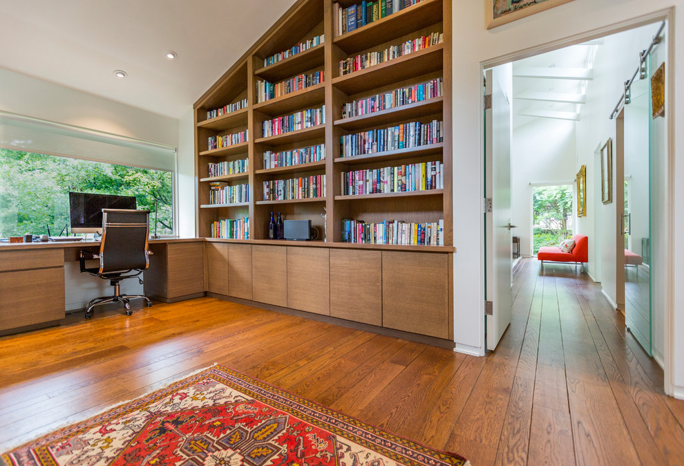Mittelgroßes Modernes Lesezimmer mit weißer Wandfarbe, braunem Holzboden, Kamin, Kaminumrandung aus Stein, Einbau-Schreibtisch und braunem Boden in Cincinnati