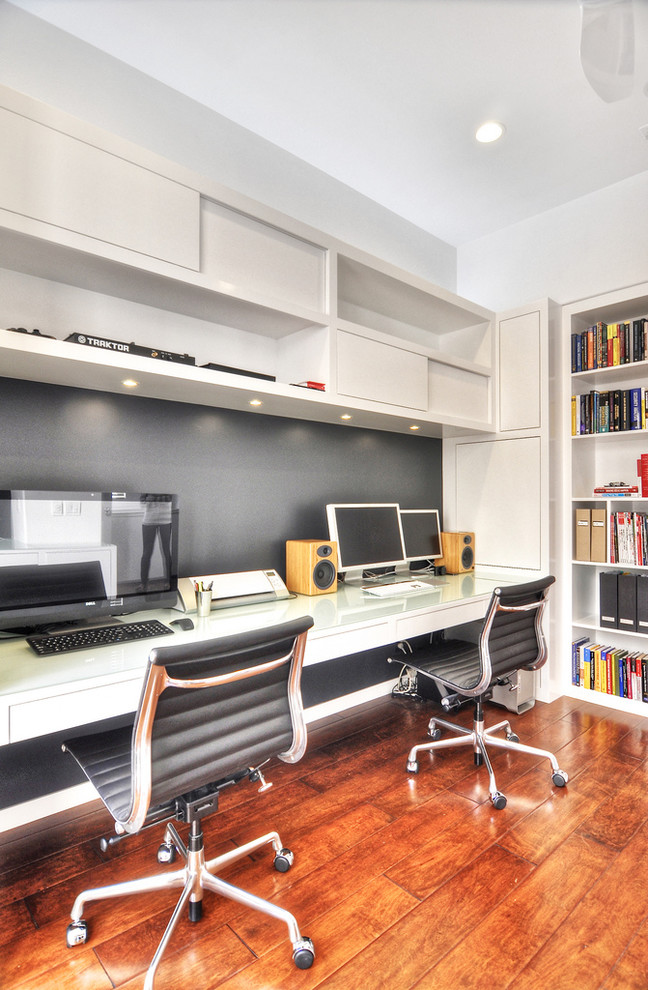 Diseño de estudio contemporáneo grande sin chimenea con paredes blancas, suelo de madera en tonos medios y escritorio empotrado