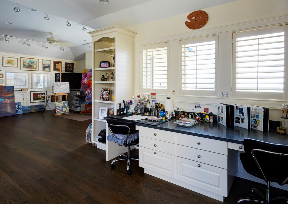 This is an example of a large craft room in Chicago with white walls, dark hardwood flooring, no fireplace, a built-in desk and brown floors.