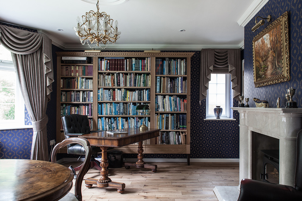 Inredning av ett klassiskt mellanstort arbetsrum, med ljust trägolv, ett fristående skrivbord, beiget golv, flerfärgade väggar, en standard öppen spis och ett bibliotek