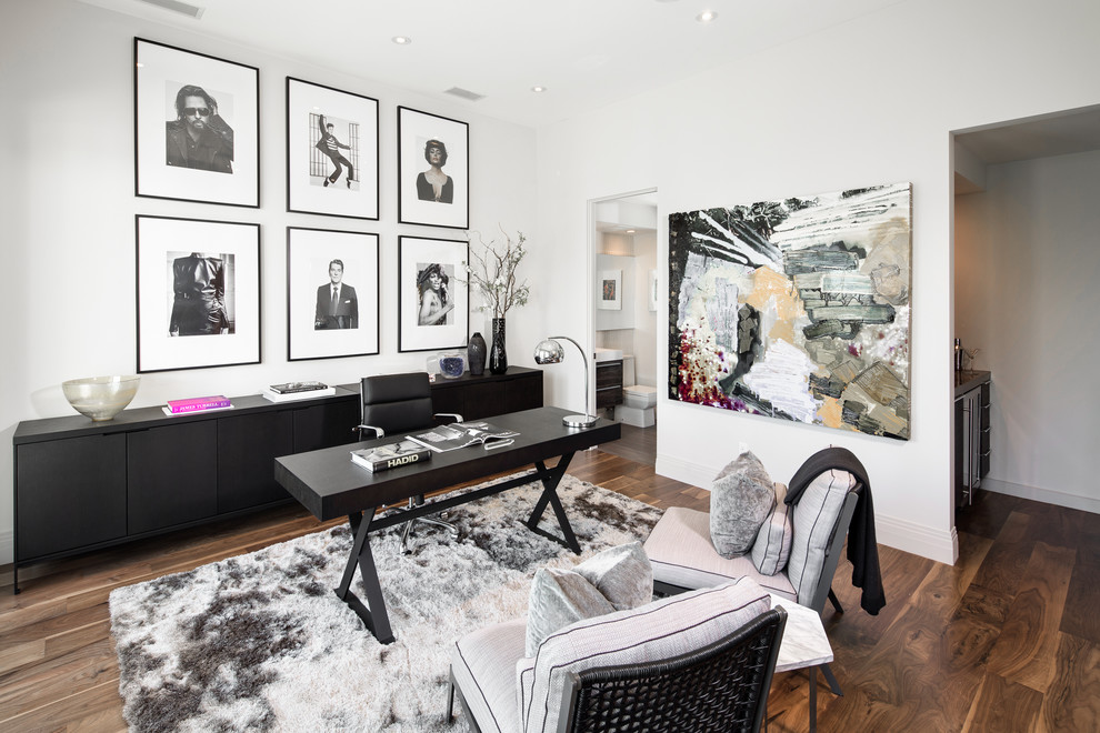 This is an example of a large contemporary study in Los Angeles with white walls, medium hardwood flooring, no fireplace, a freestanding desk and brown floors.