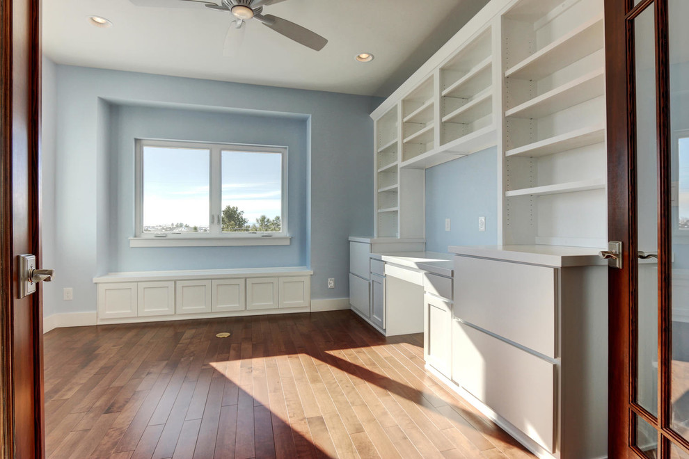 Inredning av ett amerikanskt mellanstort arbetsrum, med blå väggar, ljust trägolv och ett inbyggt skrivbord
