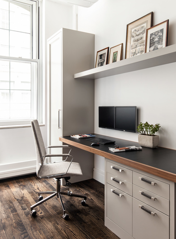 Ejemplo de despacho actual de tamaño medio sin chimenea con paredes blancas, escritorio empotrado, suelo marrón y suelo de madera oscura