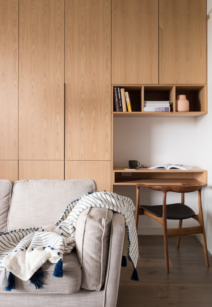 Foto de despacho actual pequeño con paredes blancas, suelo de madera en tonos medios, escritorio empotrado y suelo marrón