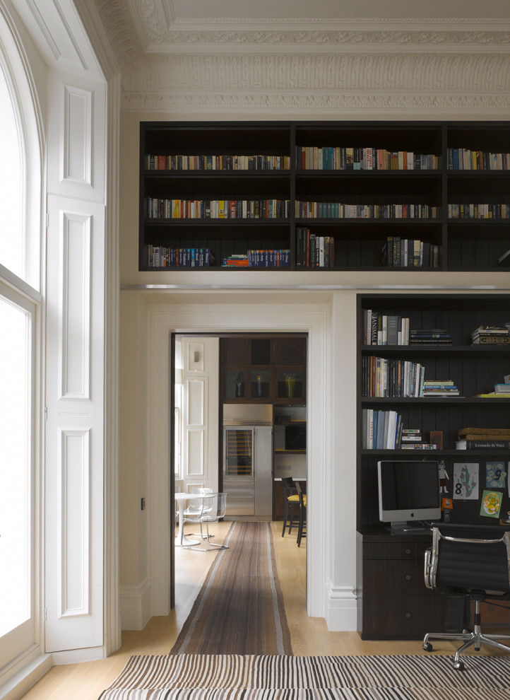 Bild på ett stort eklektiskt hemmabibliotek, med beige väggar, mellanmörkt trägolv, ett fristående skrivbord och brunt golv