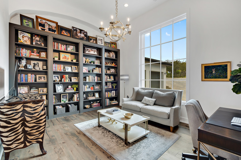 This is an example of a large mediterranean study in Austin with white walls, medium hardwood flooring, a freestanding desk and brown floors.