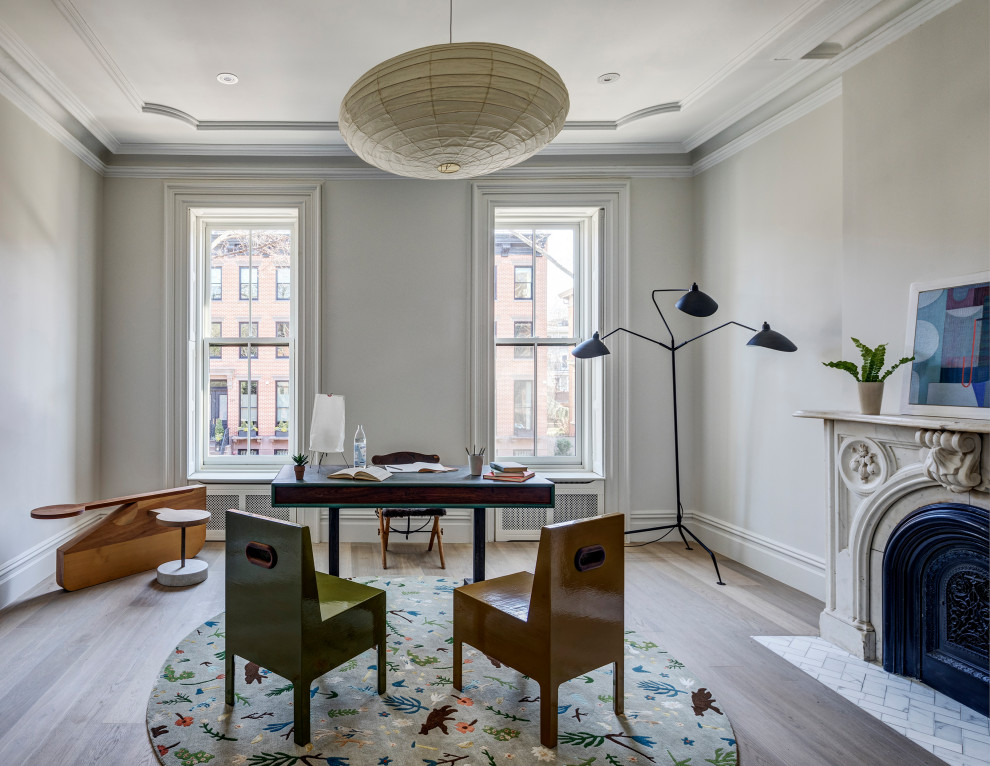 Klassisches Arbeitszimmer mit hellem Holzboden, Kamin, Kaminumrandung aus Stein, Arbeitsplatz, weißer Wandfarbe, freistehendem Schreibtisch und braunem Boden in New York