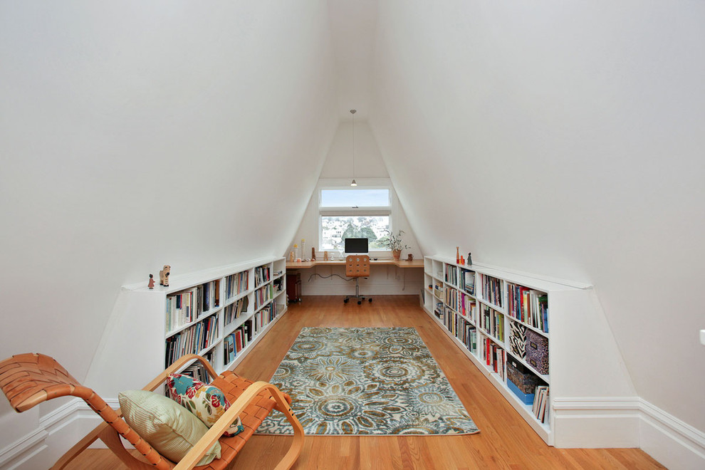 Imagen de despacho tradicional con paredes blancas, suelo de madera en tonos medios, escritorio empotrado y biblioteca