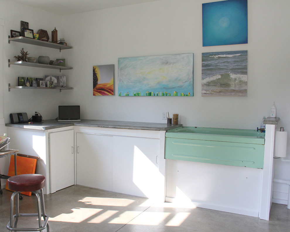 Bild på ett litet industriellt hemmastudio, med vita väggar, mörkt trägolv och ett fristående skrivbord