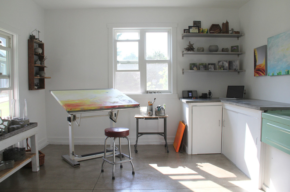 Modelo de estudio industrial pequeño sin chimenea con paredes blancas, escritorio independiente y suelo de cemento