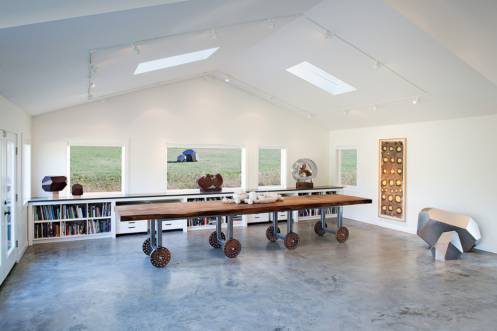 На фото: кабинет среднего размера в современном стиле с белыми стенами, бетонным полом, отдельно стоящим рабочим столом и серым полом без камина с