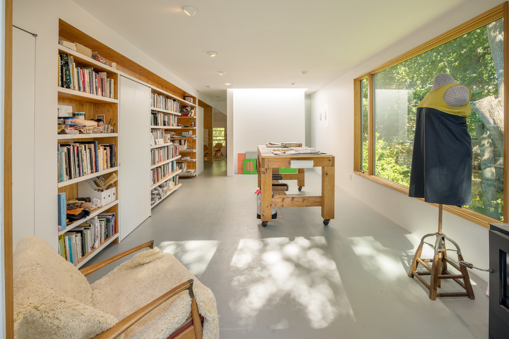 Bild på ett mellanstort funkis hemmastudio, med vita väggar, en öppen vedspis, en spiselkrans i metall, ett fristående skrivbord, grått golv och betonggolv