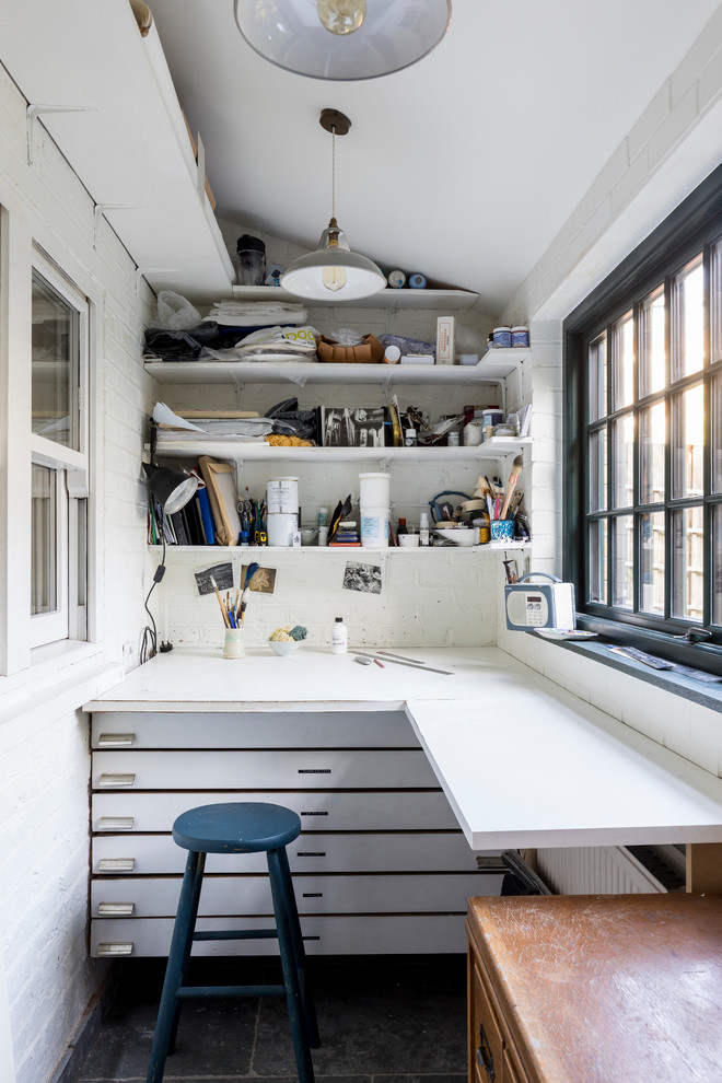 Inspiration för små industriella hobbyrum, med vita väggar, kalkstensgolv, ett inbyggt skrivbord och grått golv
