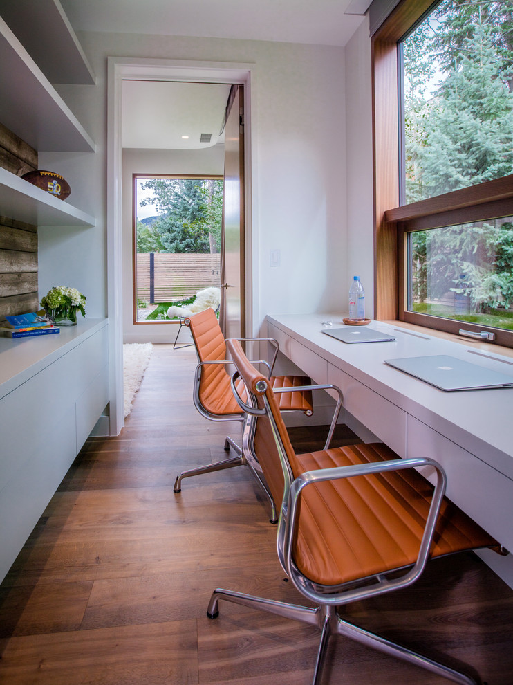Cette image montre un bureau design avec un mur blanc, un sol en bois brun, un bureau intégré et un sol marron.