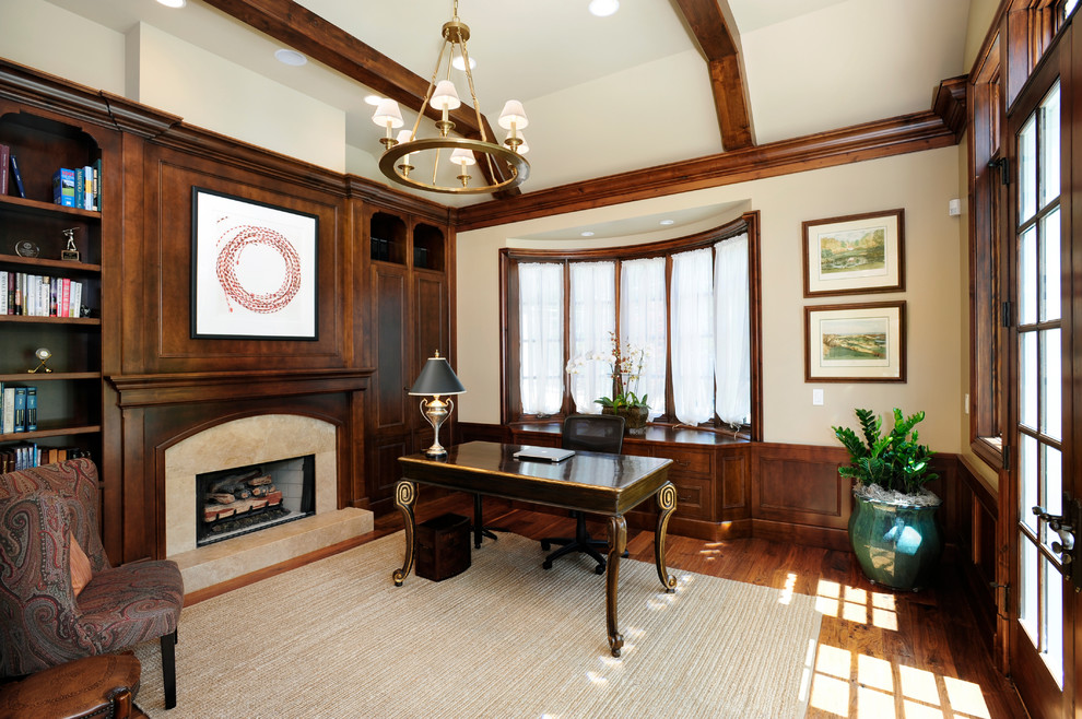 Foto de despacho tradicional extra grande con paredes beige, suelo de madera en tonos medios, todas las chimeneas, marco de chimenea de piedra y escritorio independiente