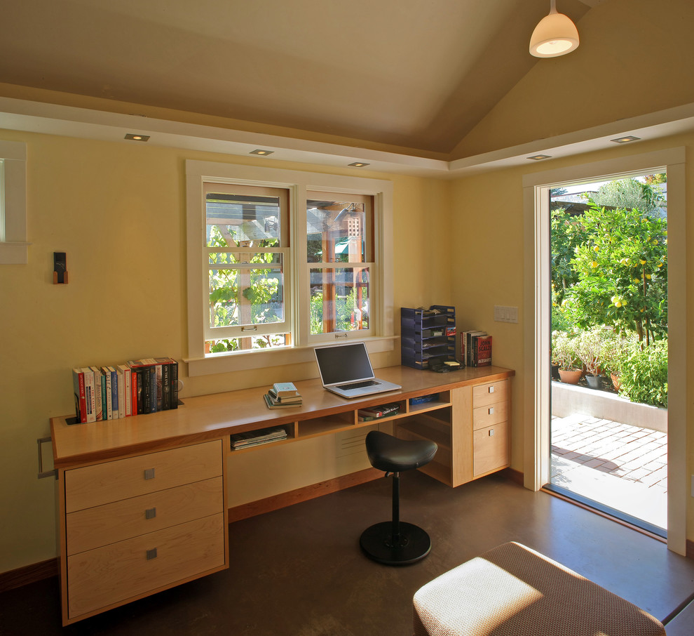 Imagen de despacho rural pequeño sin chimenea con paredes amarillas, suelo de cemento y escritorio empotrado