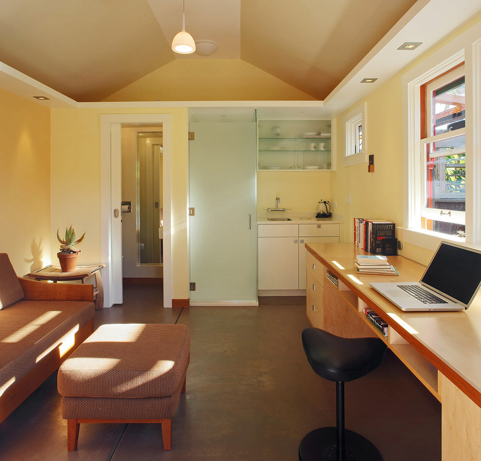 Großes Modernes Arbeitszimmer ohne Kamin mit gelber Wandfarbe, Betonboden und Einbau-Schreibtisch in San Francisco