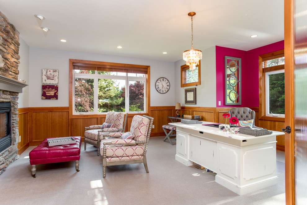 На фото: большой кабинет в стиле неоклассика (современная классика) с розовыми стенами, ковровым покрытием, стандартным камином, фасадом камина из камня и отдельно стоящим рабочим столом с