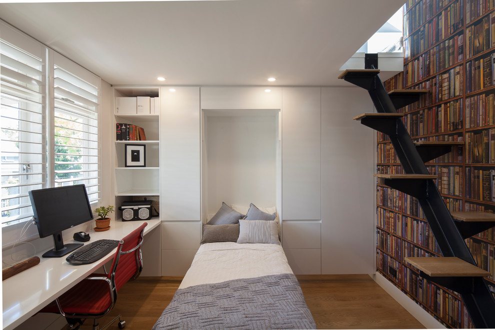 Modelo de despacho minimalista pequeño sin chimenea con escritorio empotrado, paredes blancas y suelo de madera en tonos medios