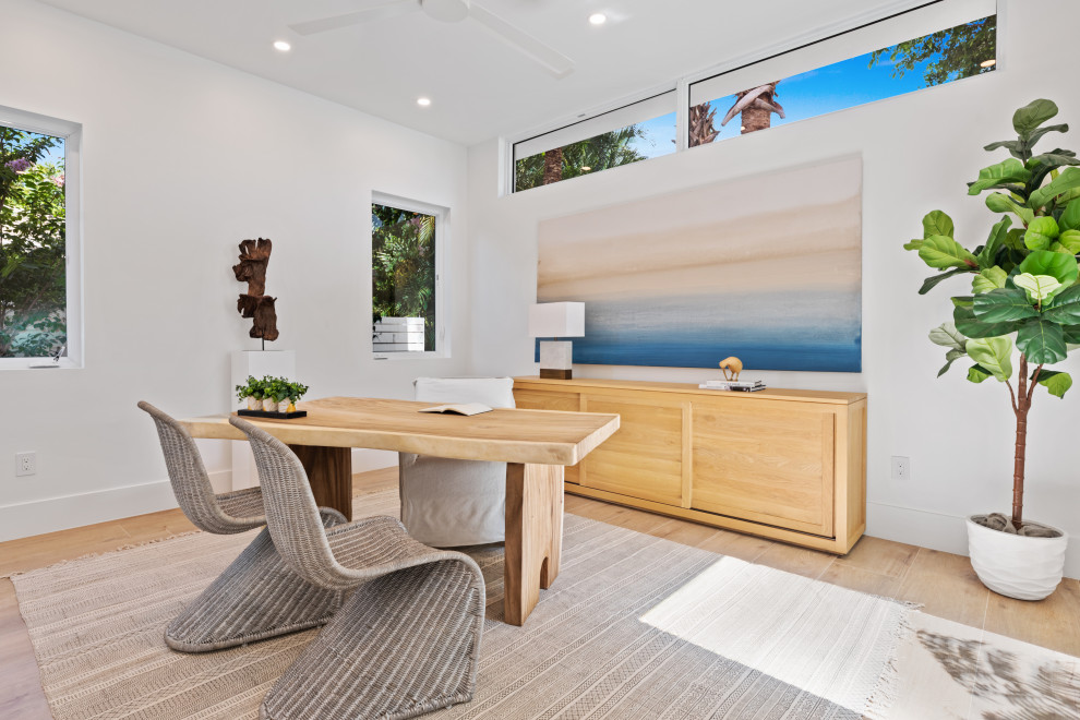 Diseño de despacho costero con paredes blancas, suelo de madera clara, escritorio independiente y suelo beige