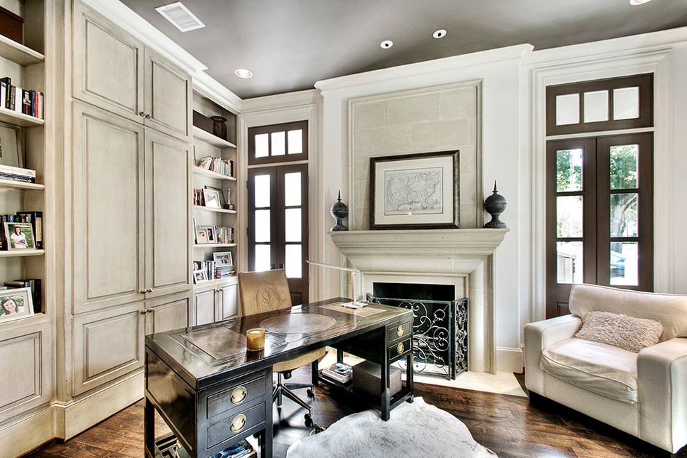 На фото: кабинет в классическом стиле с белыми стенами, темным паркетным полом, стандартным камином и отдельно стоящим рабочим столом с