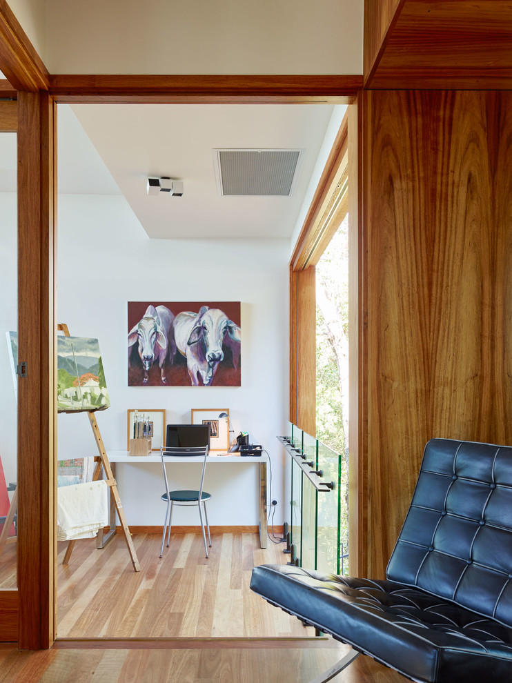 Modernes Arbeitszimmer mit weißer Wandfarbe, braunem Holzboden, freistehendem Schreibtisch und Studio in Brisbane