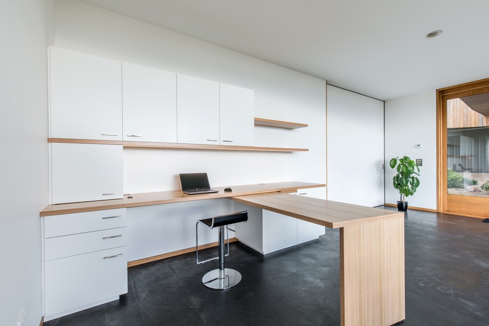 Modelo de despacho contemporáneo de tamaño medio sin chimenea con escritorio empotrado, paredes blancas y suelo de cemento