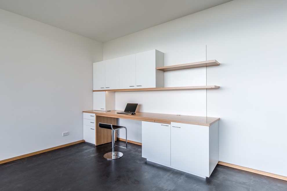 На фото: рабочее место среднего размера в современном стиле с встроенным рабочим столом, белыми стенами и бетонным полом без камина с