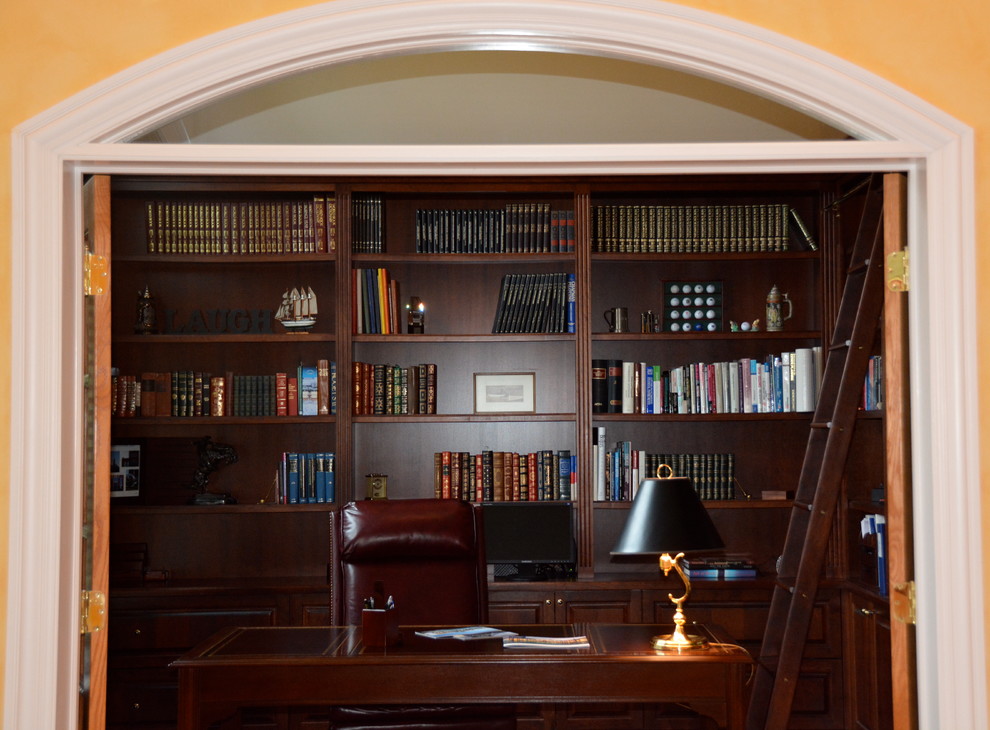 Imagen de despacho tradicional grande con biblioteca, suelo de madera en tonos medios y escritorio independiente