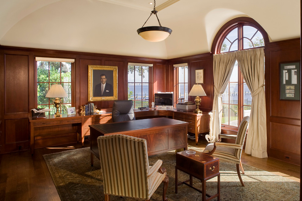 На фото: большой кабинет в классическом стиле с коричневыми стенами, паркетным полом среднего тона и отдельно стоящим рабочим столом без камина