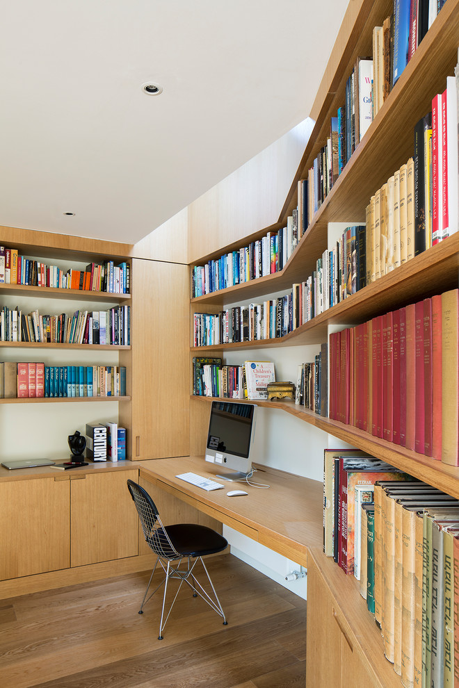 Cette photo montre un petit bureau tendance avec un mur beige, un sol en bois brun, aucune cheminée, un bureau intégré et un sol beige.