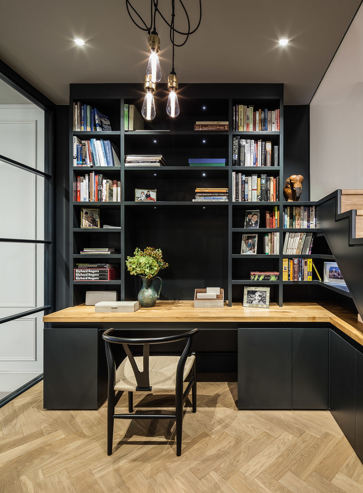 Diseño de despacho actual pequeño con paredes negras, suelo de madera clara y escritorio empotrado