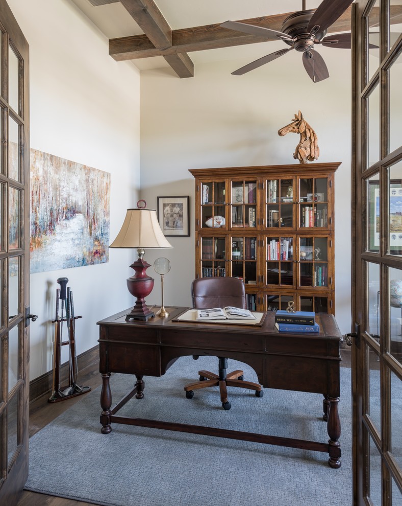 Bild på ett medelhavsstil hemmabibliotek, med beige väggar, mörkt trägolv, ett fristående skrivbord och brunt golv