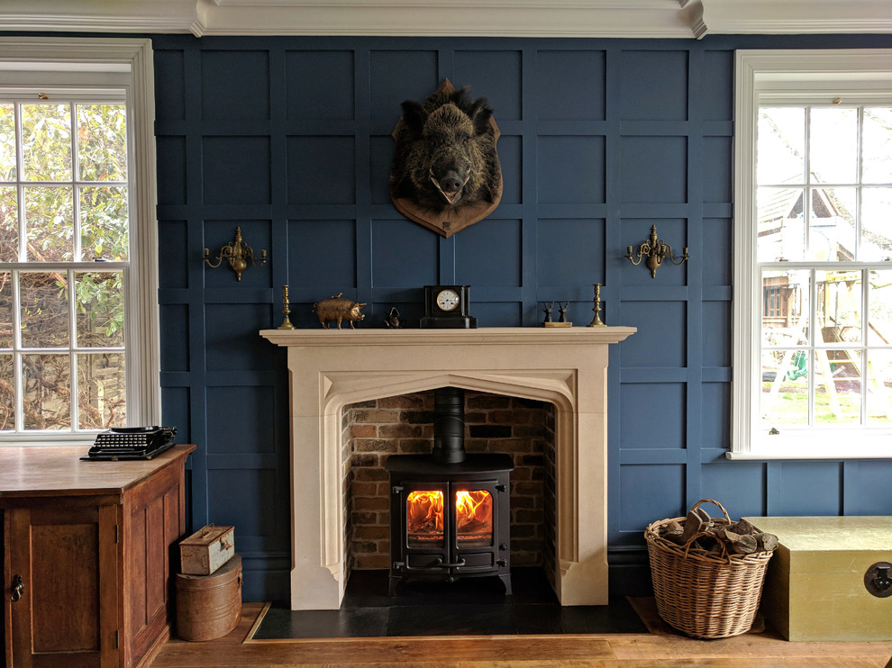 エセックスにあるお手頃価格の中くらいなトラディショナルスタイルのおしゃれな書斎 (青い壁、無垢フローリング、薪ストーブ、石材の暖炉まわり、自立型机、茶色い床) の写真
