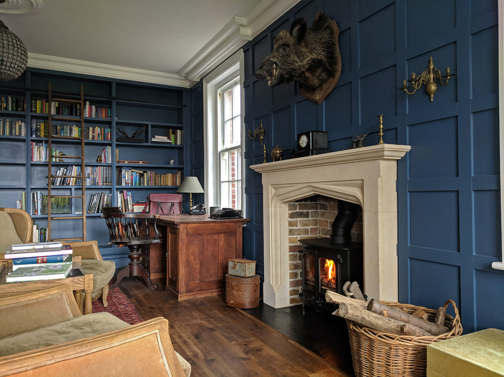 エセックスにあるお手頃価格の中くらいなトラディショナルスタイルのおしゃれな書斎 (青い壁、無垢フローリング、薪ストーブ、自立型机、茶色い床、レンガの暖炉まわり) の写真
