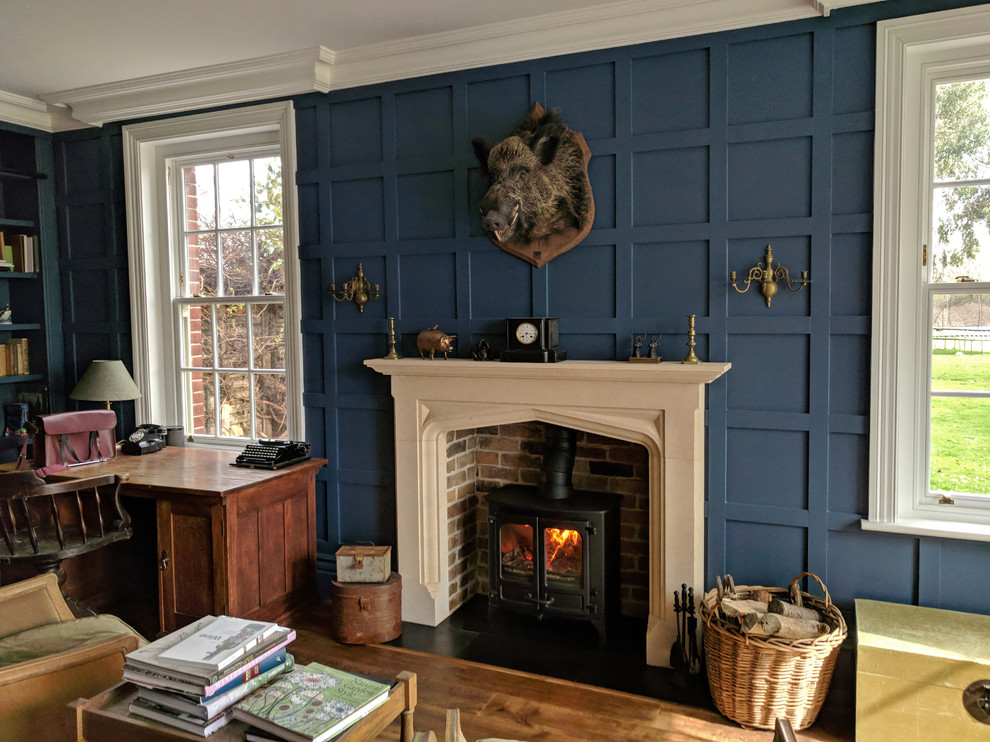 Immagine di un ufficio tradizionale di medie dimensioni con pareti blu, pavimento in legno massello medio, stufa a legna, cornice del camino in pietra, scrivania autoportante e pavimento marrone