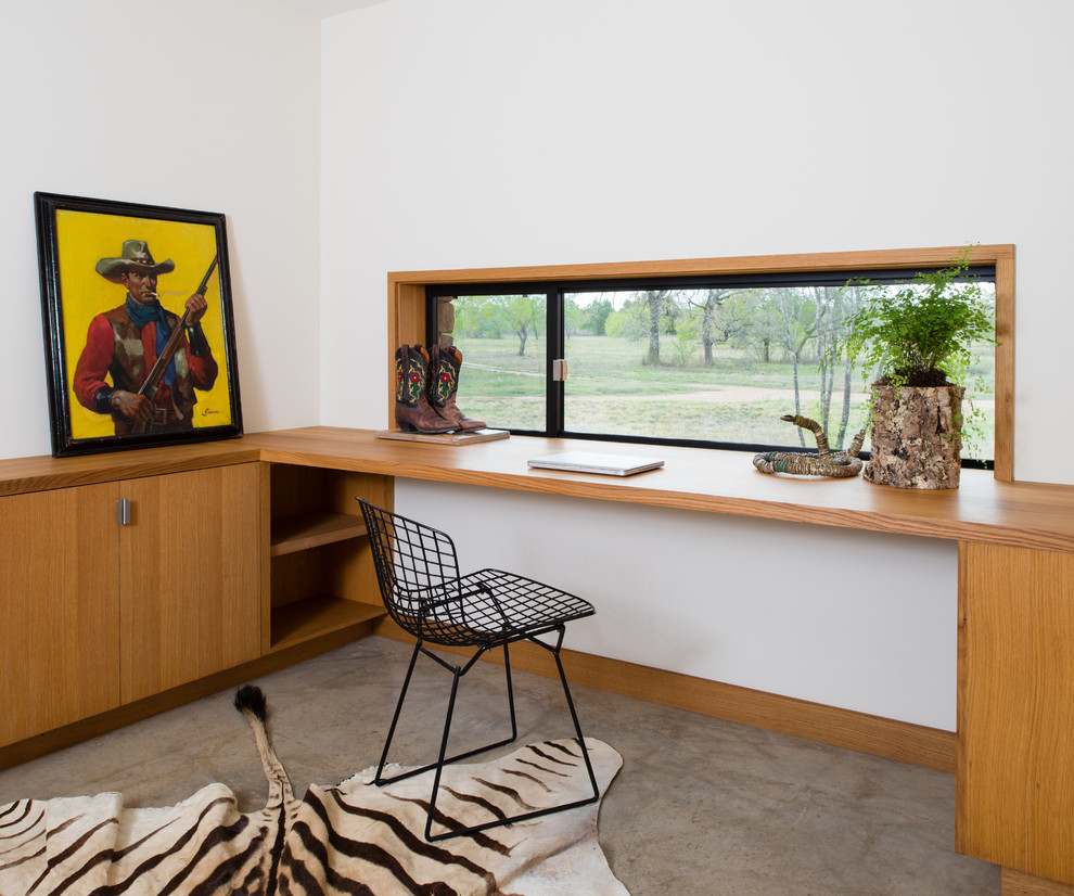 На фото: кабинет среднего размера в стиле модернизм с встроенным рабочим столом, белыми стенами, бетонным полом и коричневым полом без камина