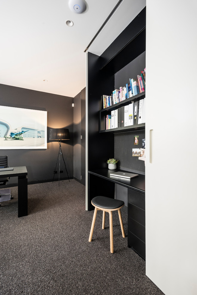 This is an example of a small modern study in Melbourne with black walls, carpet, a built-in desk and grey floors.