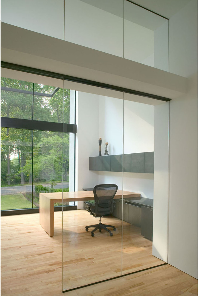 Diseño de despacho moderno de tamaño medio con paredes blancas, suelo de madera clara y escritorio empotrado
