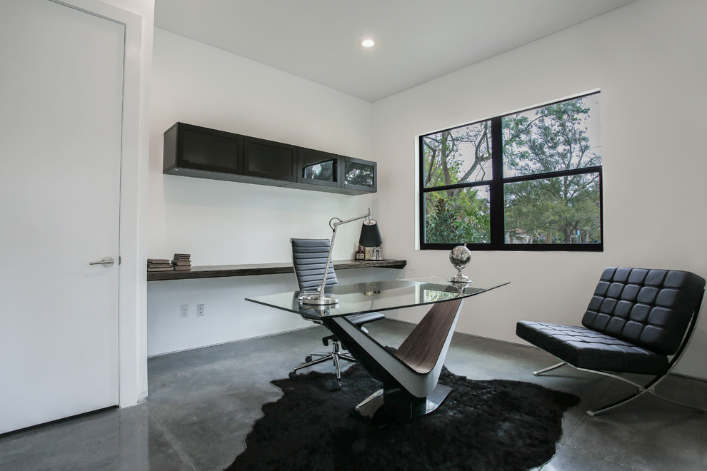 Esempio di uno studio minimal di medie dimensioni con pareti bianche, pavimento in cemento e scrivania autoportante