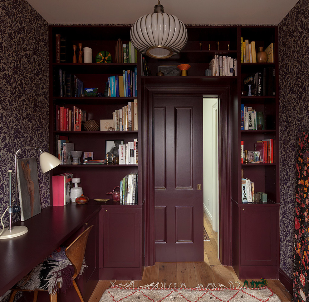 Diseño de despacho clásico renovado con paredes púrpuras, suelo de madera en tonos medios, escritorio empotrado y biblioteca