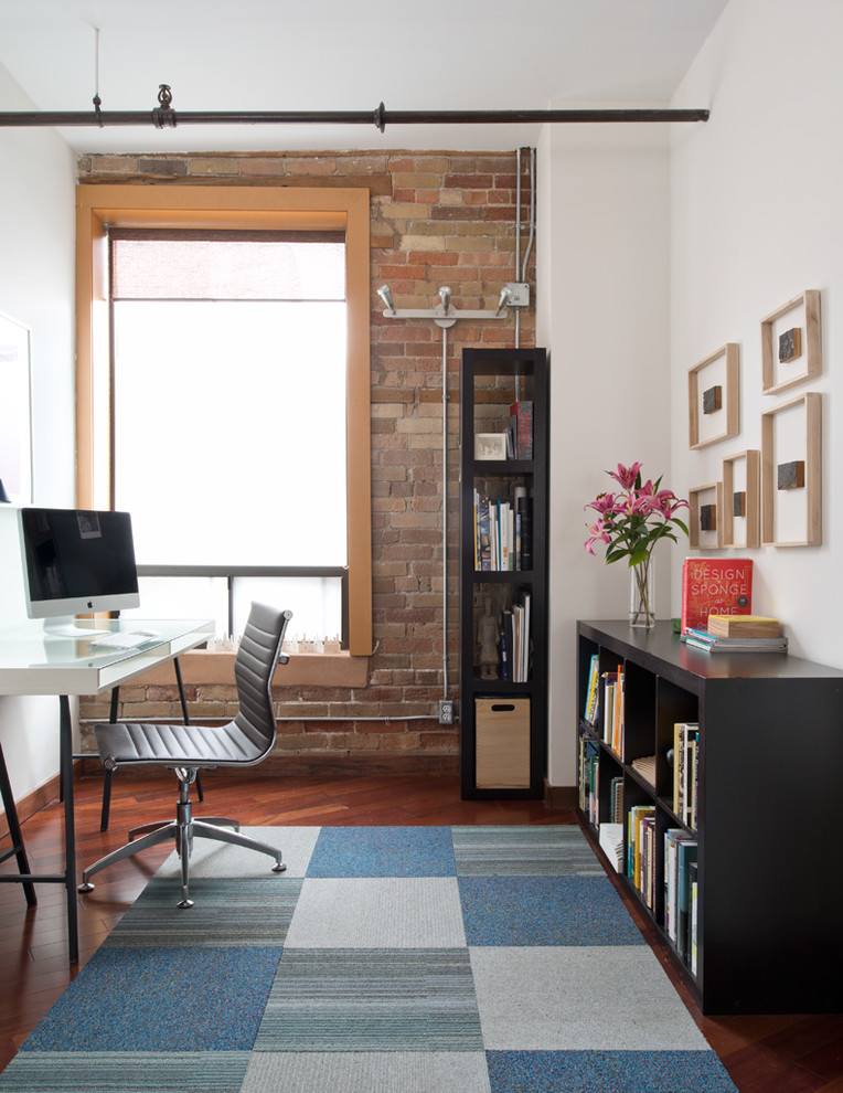 Diseño de despacho urbano con paredes blancas, escritorio independiente y suelo de madera oscura