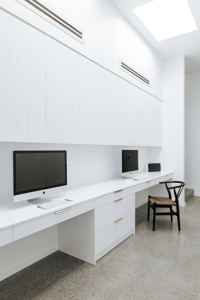 Ejemplo de despacho minimalista de tamaño medio con paredes blancas, suelo de cemento, escritorio empotrado y suelo gris