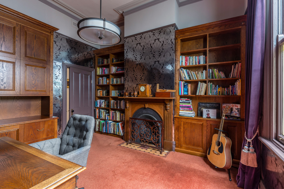 Exempel på ett mellanstort klassiskt hemmabibliotek, med grå väggar, heltäckningsmatta, en standard öppen spis, en spiselkrans i trä, ett fristående skrivbord och orange golv
