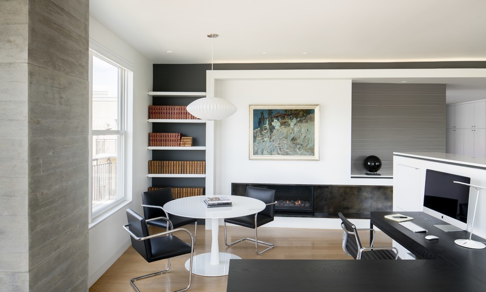 Modelo de despacho moderno de tamaño medio con paredes blancas, suelo de madera clara, chimenea lineal, marco de chimenea de yeso, escritorio empotrado y suelo beige