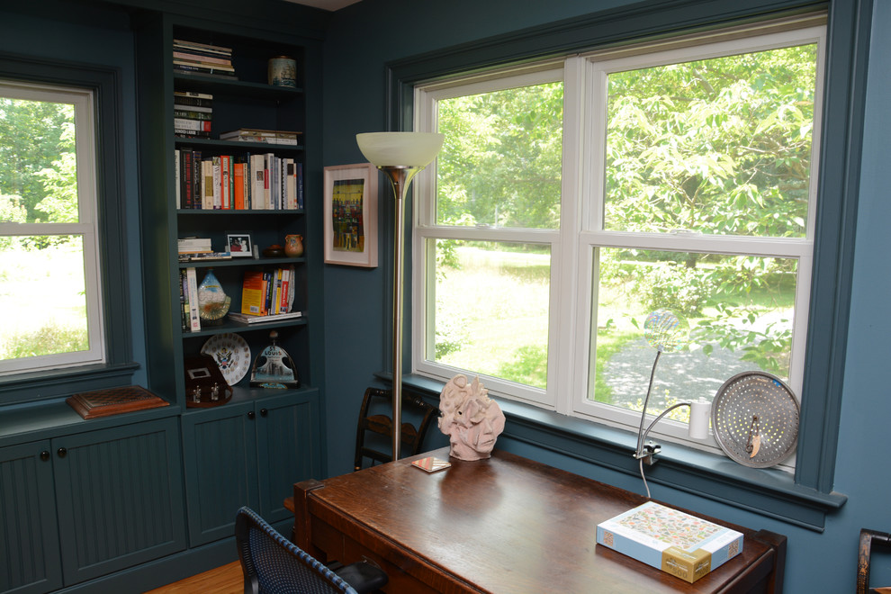 Inredning av ett klassiskt mellanstort arbetsrum, med ett bibliotek, blå väggar, ljust trägolv, ett fristående skrivbord och brunt golv